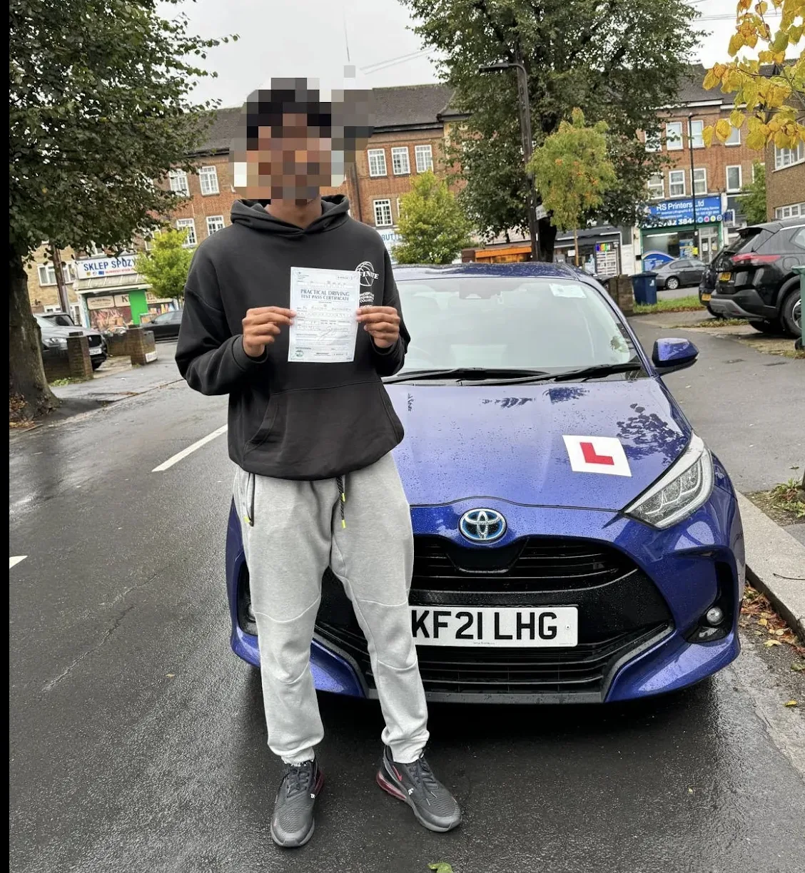 Successful driving test candidate holding pass certificate outside DVSA test centre in Pinner area, North London